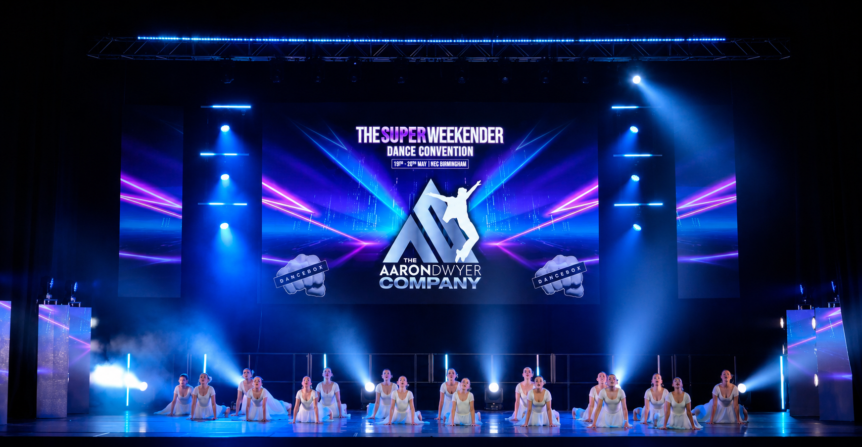 AD dancers performing across a blue-lit theatre stage beneath The Aaron Dwyer Company screen.