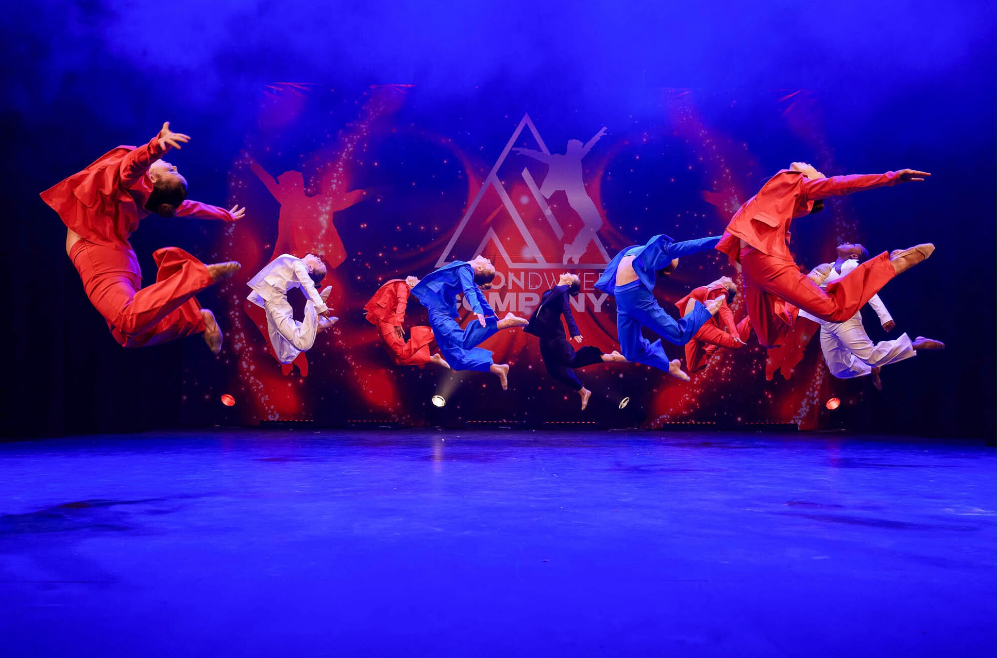 Dancers in red, white and blue costumes leaping across the stage.