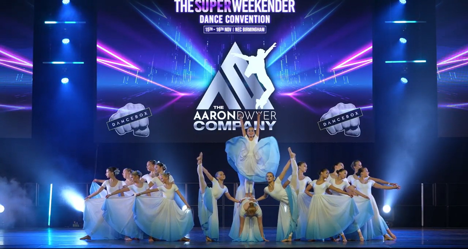 AD dancers performing in formation beneath the Aaron Dwyer Company stage backdrop.